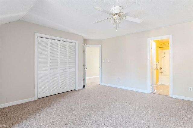 unfurnished bedroom featuring a closet, ensuite bathroom, light colored carpet, and ceiling fan