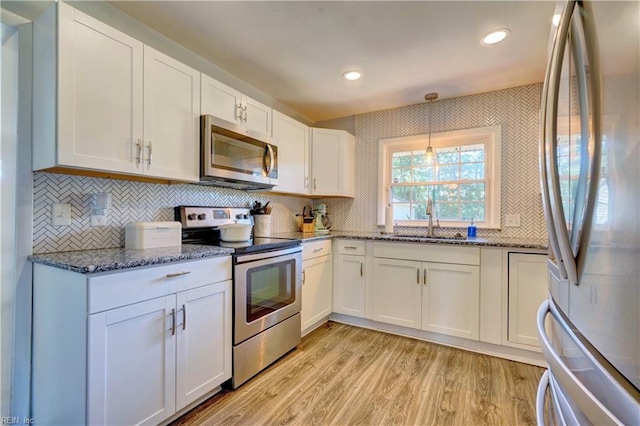 kitchen with hanging light fixtures, sink, light wood-type flooring, white cabinetry, and appliances with stainless steel finishes