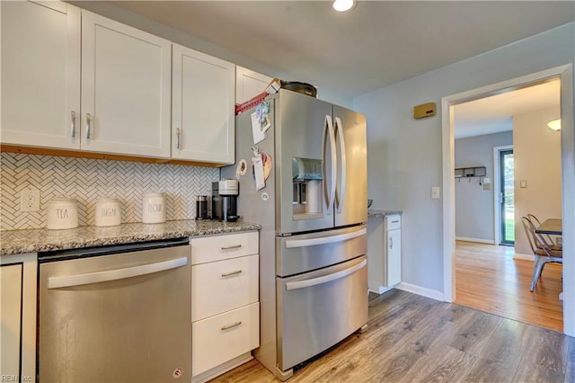 kitchen featuring decorative backsplash, white cabinetry, light stone countertops, light wood-type flooring, and stainless steel appliances