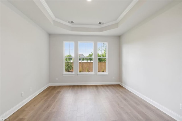 empty room featuring ornamental molding, a tray ceiling, and light wood-type flooring