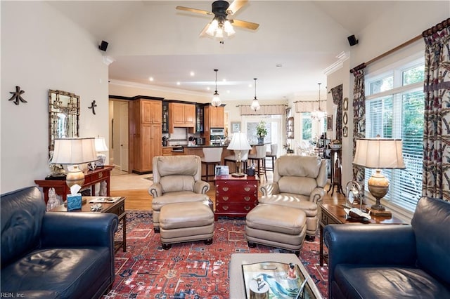 living room with ornamental molding, light wood-type flooring, ceiling fan with notable chandelier, and vaulted ceiling