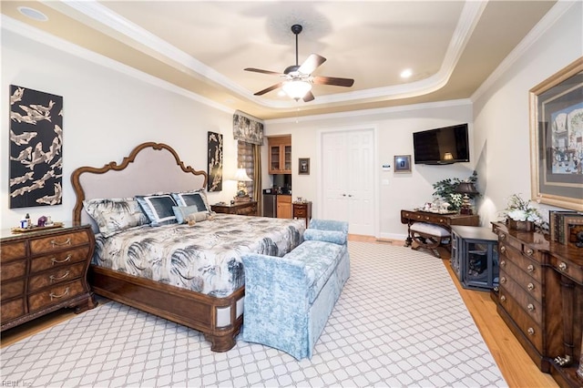 bedroom with a closet, a tray ceiling, crown molding, light hardwood / wood-style floors, and ceiling fan