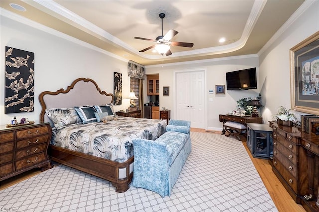 bedroom featuring ceiling fan, a tray ceiling, light wood-type flooring, ornamental molding, and a closet