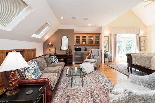 living room featuring vaulted ceiling with skylight, french doors, and light wood-type flooring