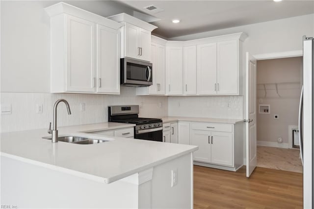 kitchen featuring kitchen peninsula, white cabinets, light wood-type flooring, sink, and stainless steel appliances