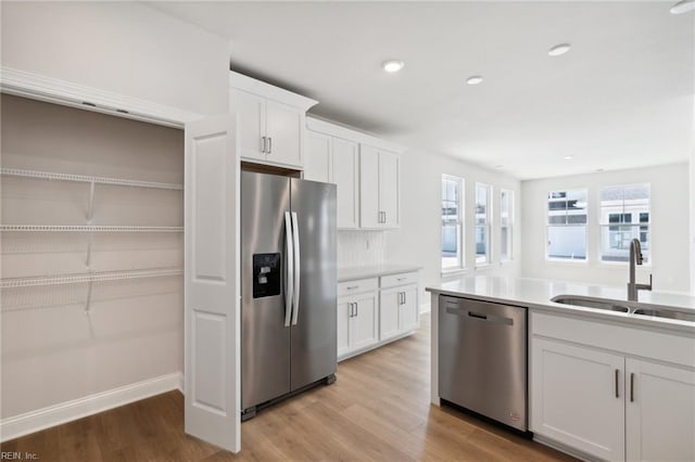 kitchen with appliances with stainless steel finishes, white cabinetry, sink, and light wood-type flooring