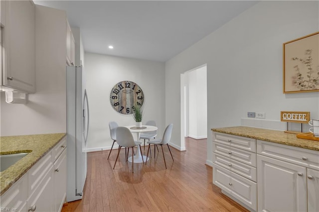 kitchen with light stone countertops, white cabinetry, white fridge, and light hardwood / wood-style floors