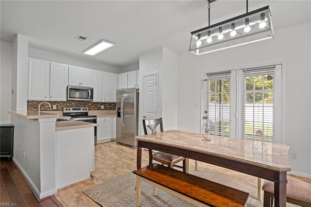 kitchen with appliances with stainless steel finishes, kitchen peninsula, pendant lighting, white cabinetry, and backsplash