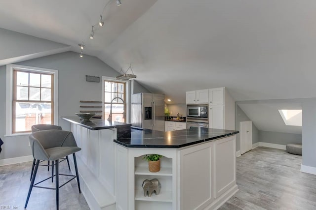 kitchen with white cabinets, a breakfast bar area, appliances with stainless steel finishes, light hardwood / wood-style flooring, and vaulted ceiling with skylight