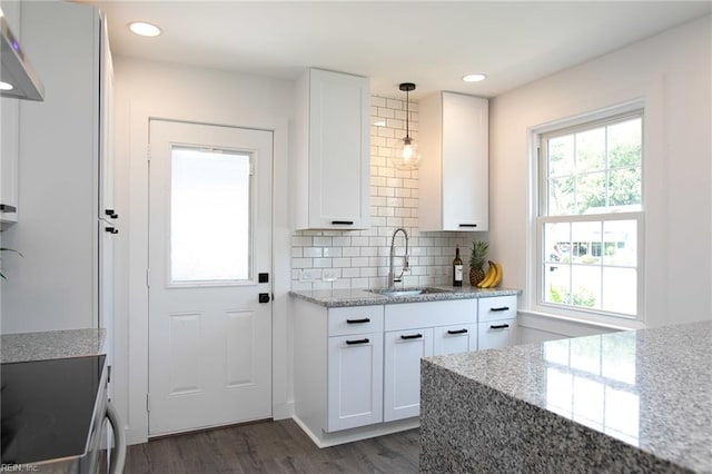 kitchen featuring light stone counters, sink, white cabinets, and hanging light fixtures