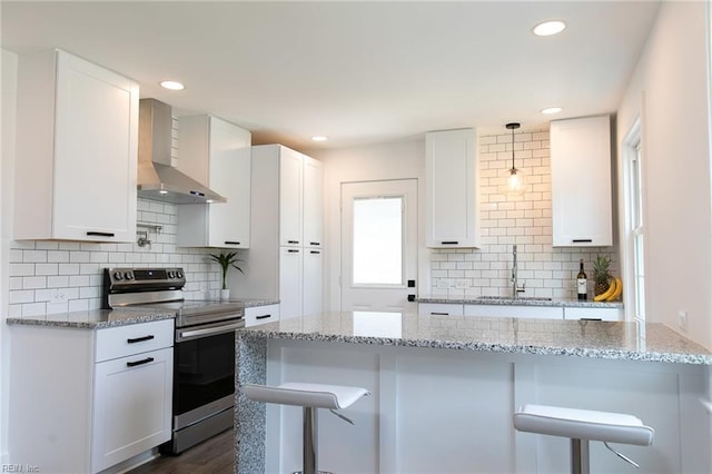 kitchen featuring electric range, white cabinetry, wall chimney exhaust hood, and a breakfast bar area