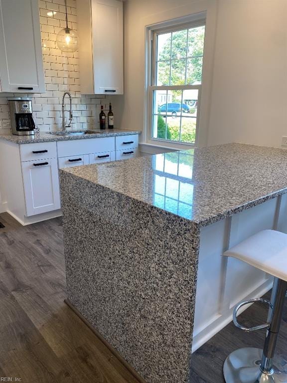 kitchen with backsplash, a kitchen breakfast bar, sink, dark hardwood / wood-style floors, and white cabinetry