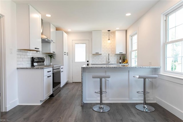 kitchen featuring white cabinetry, dark wood-type flooring, light stone counters, a kitchen bar, and electric stove