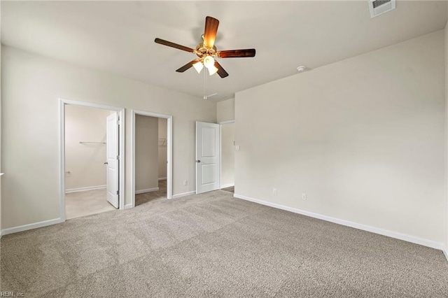 unfurnished bedroom featuring ensuite bathroom, a spacious closet, a closet, ceiling fan, and light carpet