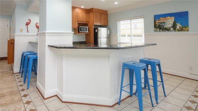 kitchen with a breakfast bar area, ornamental molding, stainless steel appliances, and light tile patterned floors