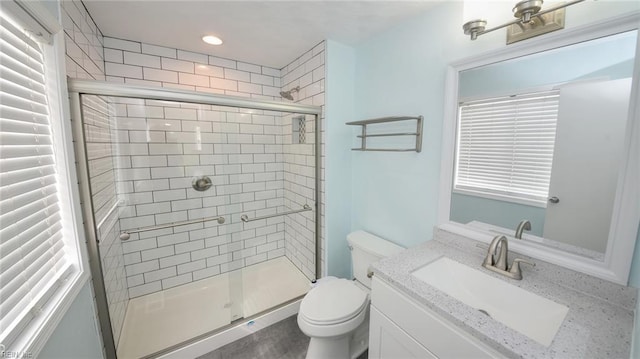 bathroom featuring a shower with door, vanity, and toilet