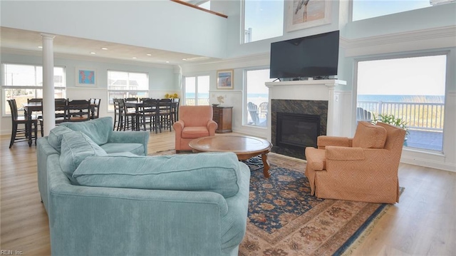 living room featuring a towering ceiling, light hardwood / wood-style flooring, a high end fireplace, and decorative columns