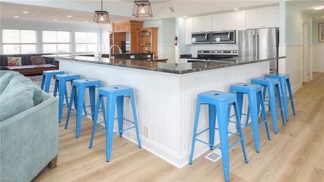 kitchen featuring stainless steel appliances, decorative light fixtures, a kitchen bar, and white cabinets