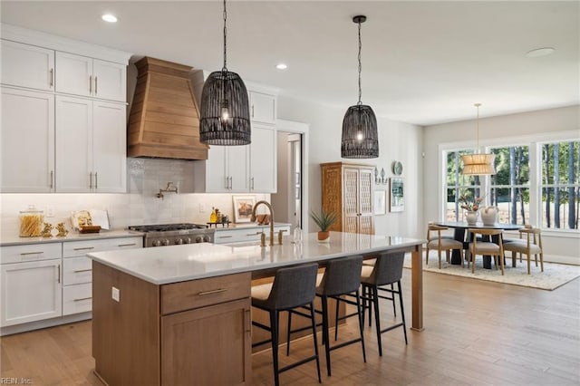 kitchen featuring premium range hood, a kitchen island with sink, white cabinetry, and light hardwood / wood-style floors