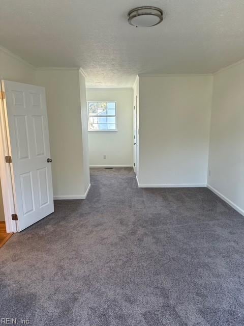 spare room with crown molding, a textured ceiling, and dark carpet