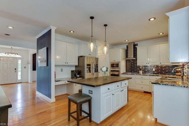 kitchen featuring wall chimney range hood, appliances with stainless steel finishes, a kitchen island, light hardwood / wood-style floors, and white cabinets