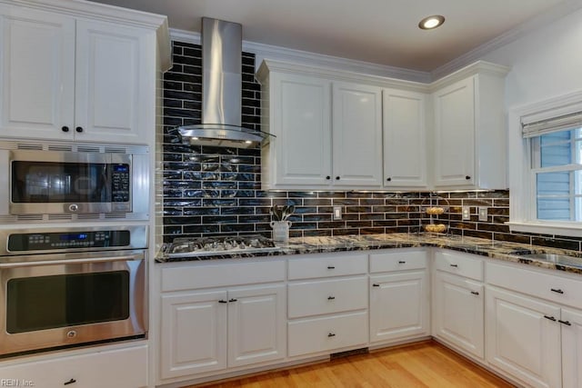 kitchen with white cabinetry, stainless steel appliances, wall chimney exhaust hood, and decorative backsplash