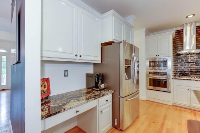 kitchen with appliances with stainless steel finishes, wall chimney exhaust hood, white cabinetry, and light hardwood / wood-style floors