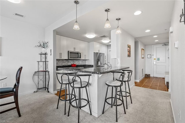 kitchen with hanging light fixtures, dark stone counters, light colored carpet, white cabinetry, and appliances with stainless steel finishes