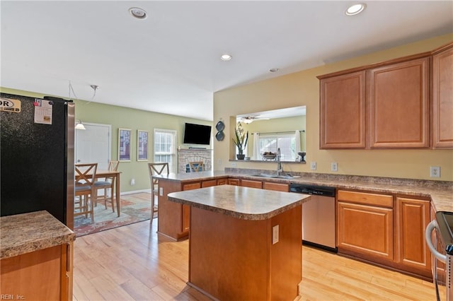 kitchen with stainless steel appliances, sink, a fireplace, light hardwood / wood-style floors, and a center island