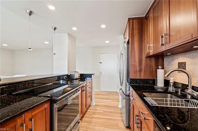 kitchen with light wood-type flooring, dark stone countertops, sink, pendant lighting, and stainless steel appliances