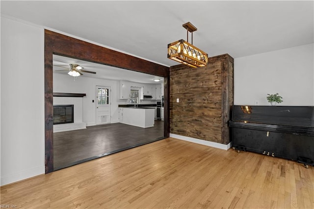 unfurnished living room featuring light hardwood / wood-style flooring, sink, a fireplace, and ceiling fan