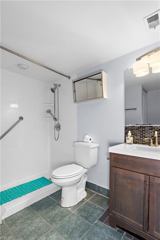 bathroom featuring vanity, toilet, a shower, and backsplash