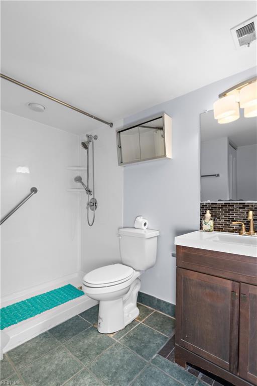 bathroom featuring vanity, backsplash, toilet, and walk in shower