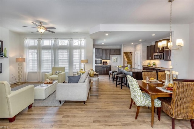 living room with light wood-type flooring and ceiling fan with notable chandelier