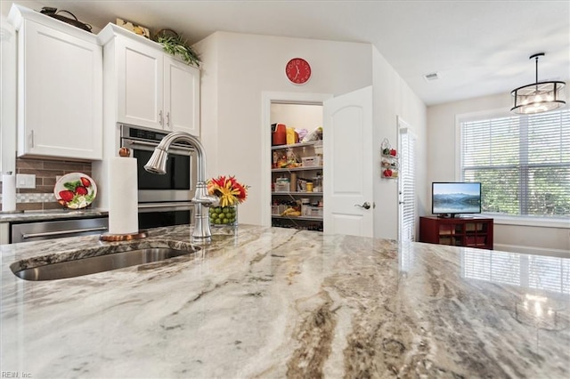 kitchen featuring backsplash, stainless steel oven, light stone countertops, and white cabinets