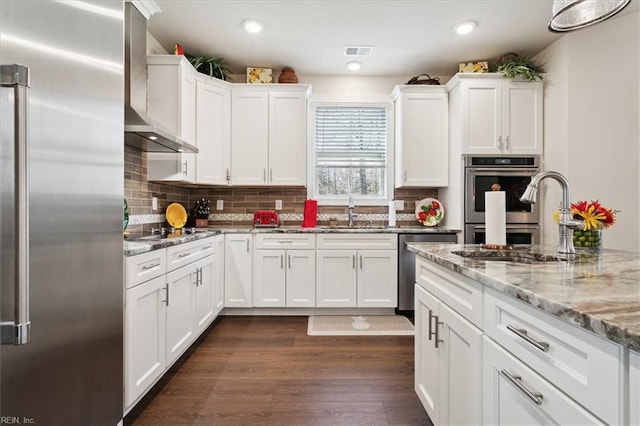 kitchen with appliances with stainless steel finishes, wall chimney exhaust hood, and white cabinets