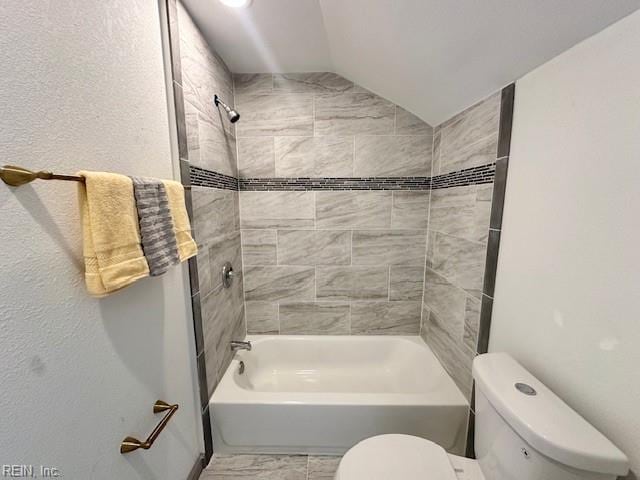 bathroom with tiled shower / bath, lofted ceiling, and toilet