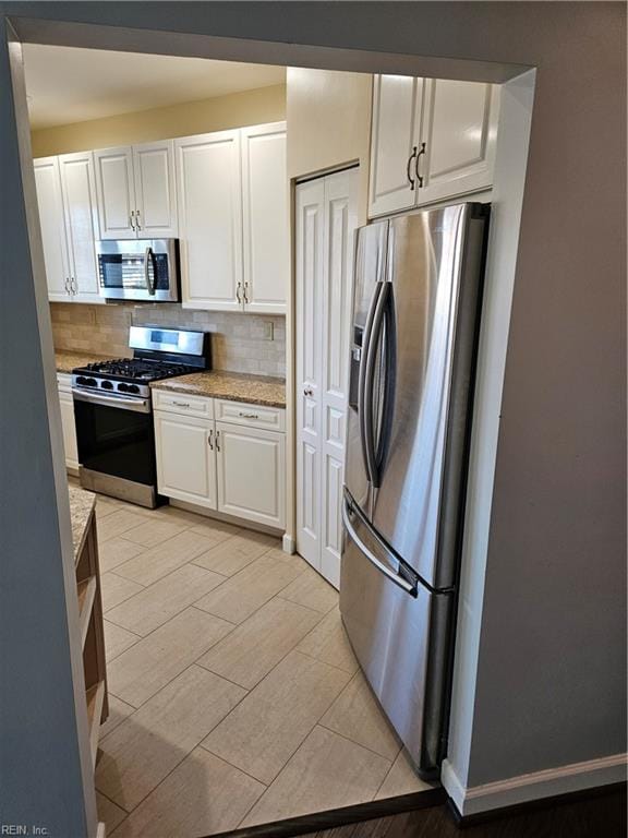 kitchen with backsplash, light stone countertops, light tile patterned flooring, white cabinetry, and stainless steel appliances