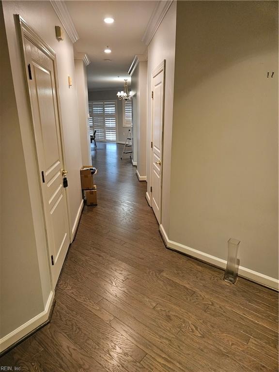 hallway with crown molding, dark wood-type flooring, and an inviting chandelier