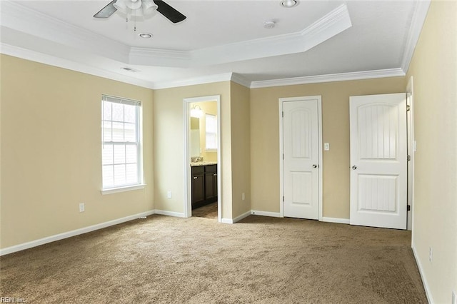 unfurnished bedroom with ornamental molding, ensuite bath, dark carpet, and a raised ceiling