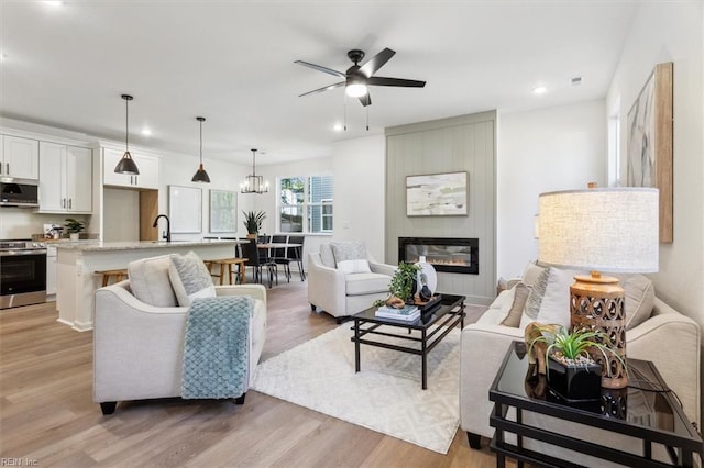 living room featuring sink, light hardwood / wood-style flooring, a fireplace, and ceiling fan with notable chandelier