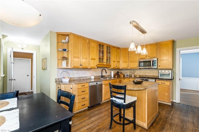 kitchen featuring appliances with stainless steel finishes, a kitchen island, pendant lighting, light stone counters, and dark hardwood / wood-style floors