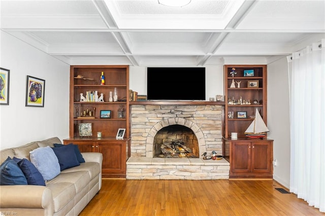 living room with a stone fireplace, coffered ceiling, wood-type flooring, and beamed ceiling