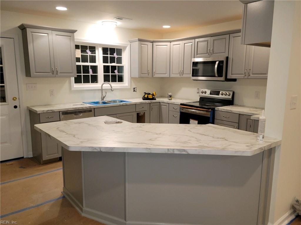 kitchen with gray cabinetry, light stone countertops, sink, kitchen peninsula, and stainless steel appliances