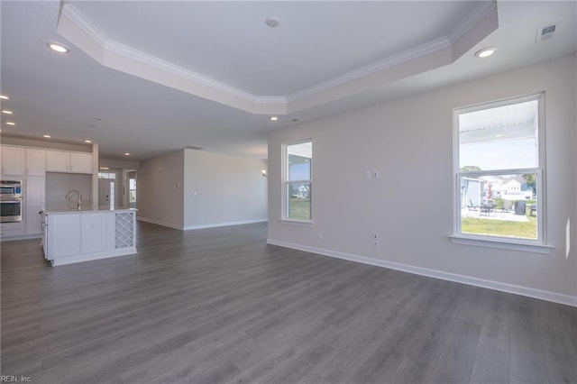 unfurnished living room featuring a tray ceiling, sink, dark hardwood / wood-style floors, and ornamental molding