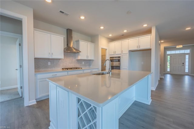 kitchen with wall chimney exhaust hood, dark hardwood / wood-style floors, white cabinetry, and a kitchen island with sink