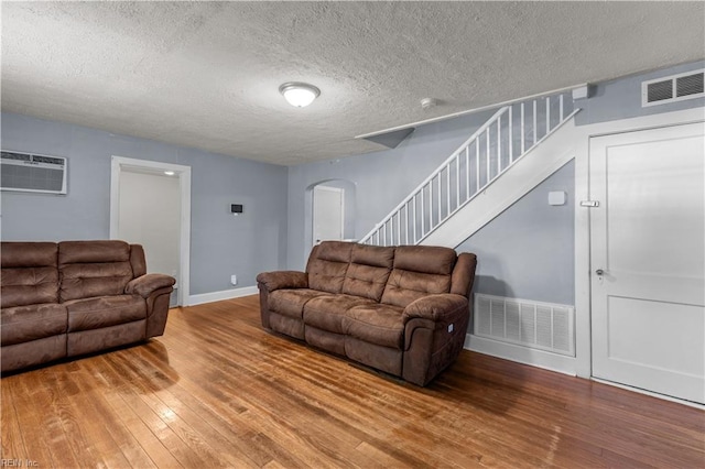 living room with an AC wall unit, hardwood / wood-style flooring, and a textured ceiling