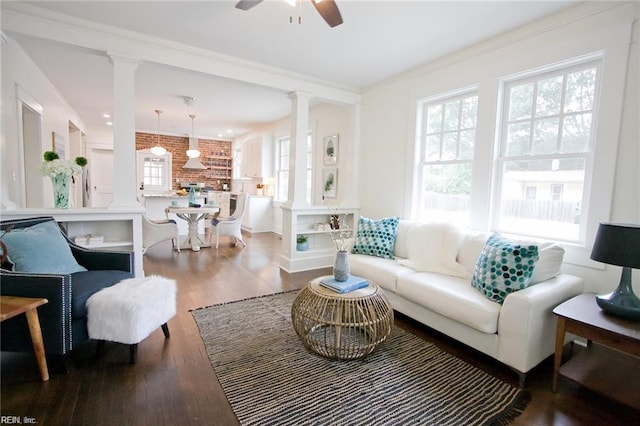 living room with decorative columns, ceiling fan, crown molding, hardwood / wood-style flooring, and brick wall