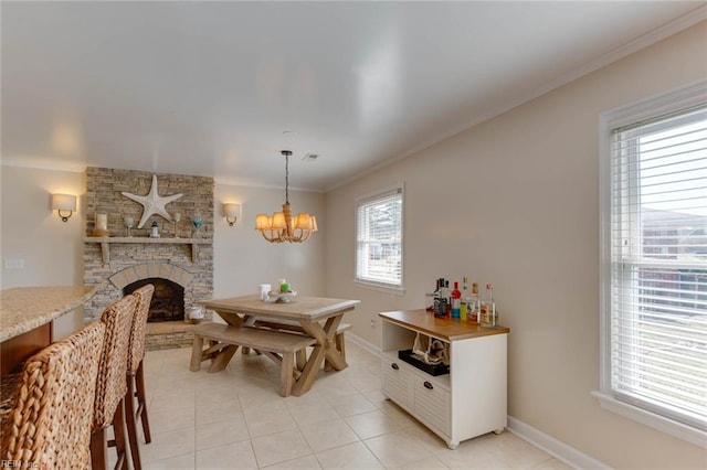 dining space with a stone fireplace, crown molding, an inviting chandelier, and light tile patterned floors