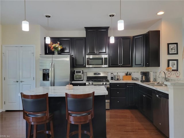 kitchen with sink, appliances with stainless steel finishes, decorative light fixtures, and dark hardwood / wood-style floors